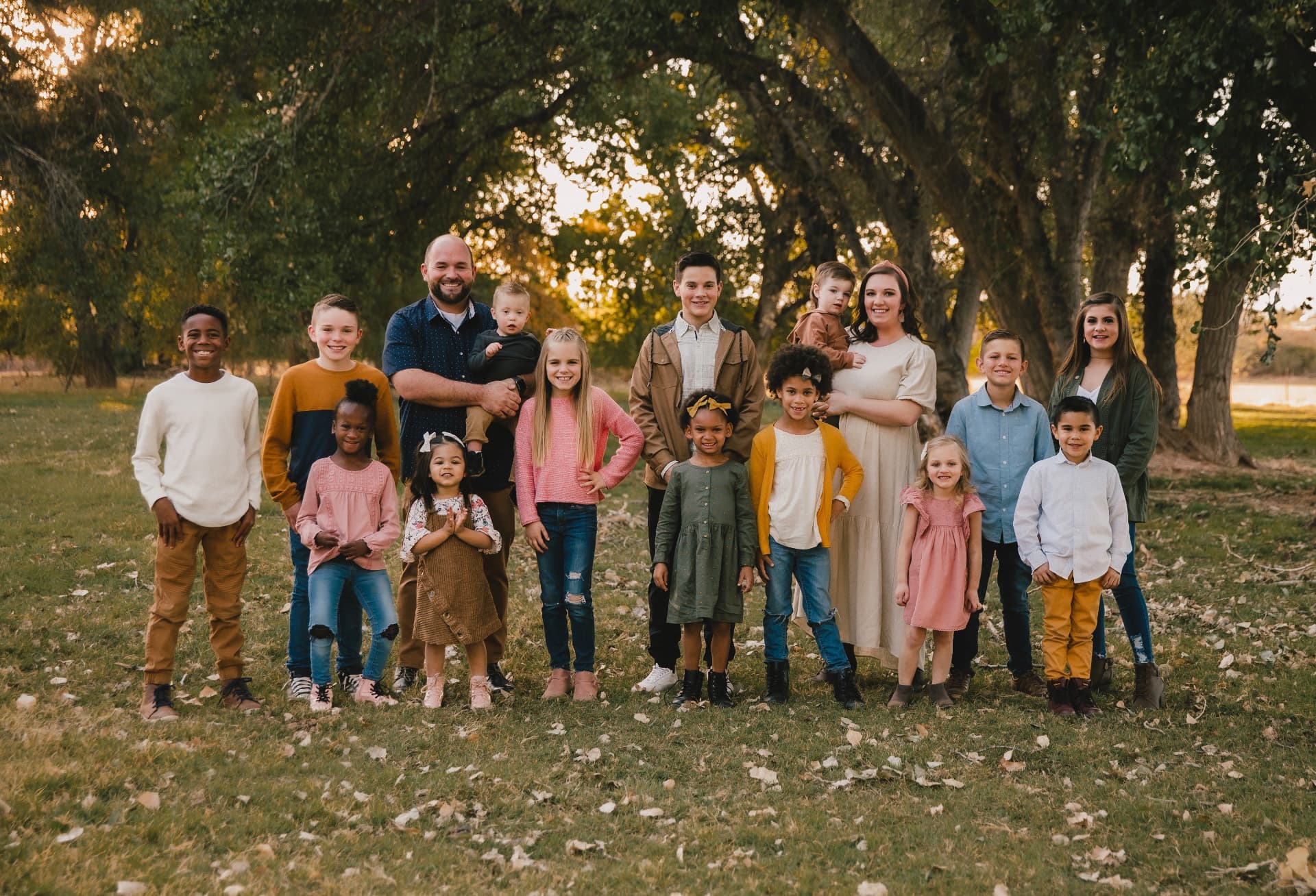 Nick, his wife and their sixteen children standing together outdoors under the trees